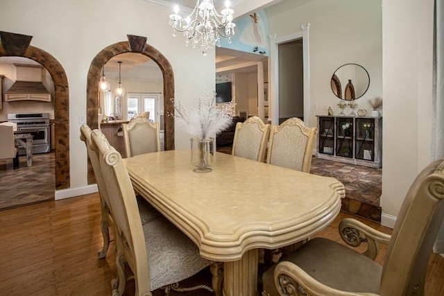 dining area featuring a chandelier, wood finished floors, arched walkways, and baseboards