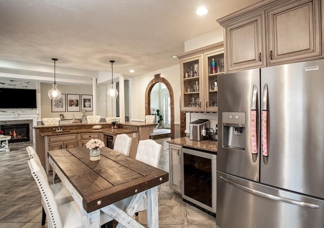 kitchen featuring stainless steel fridge with ice dispenser, wine cooler, arched walkways, a glass covered fireplace, and open floor plan