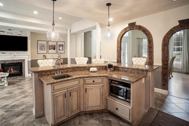 kitchen featuring a sink, stainless steel microwave, open floor plan, a kitchen island with sink, and light stone countertops