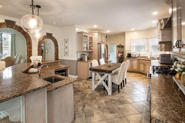 kitchen featuring a sink, stainless steel fridge with ice dispenser, glass insert cabinets, dark stone countertops, and recessed lighting