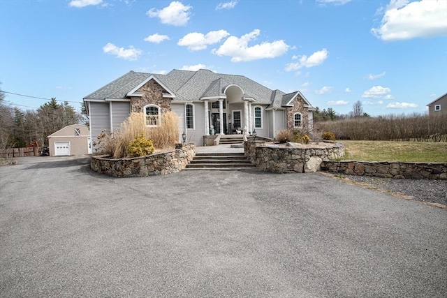 ranch-style home featuring an outdoor structure, a detached garage, asphalt driveway, and roof with shingles