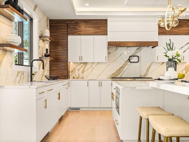 kitchen with light stone countertops, white cabinetry, decorative backsplash, sink, and a breakfast bar area