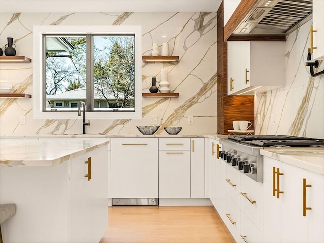 kitchen with stainless steel gas stovetop, custom exhaust hood, sink, white cabinets, and light stone countertops