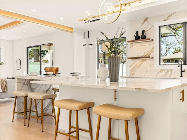 kitchen with light stone counters, backsplash, a kitchen bar, and light hardwood / wood-style floors