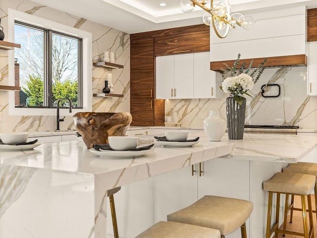 kitchen with pendant lighting, a kitchen bar, white cabinetry, tasteful backsplash, and sink