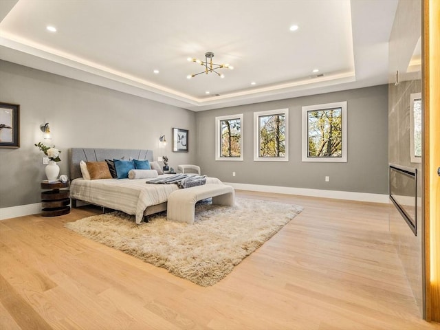 bedroom with light hardwood / wood-style floors, an inviting chandelier, and a raised ceiling