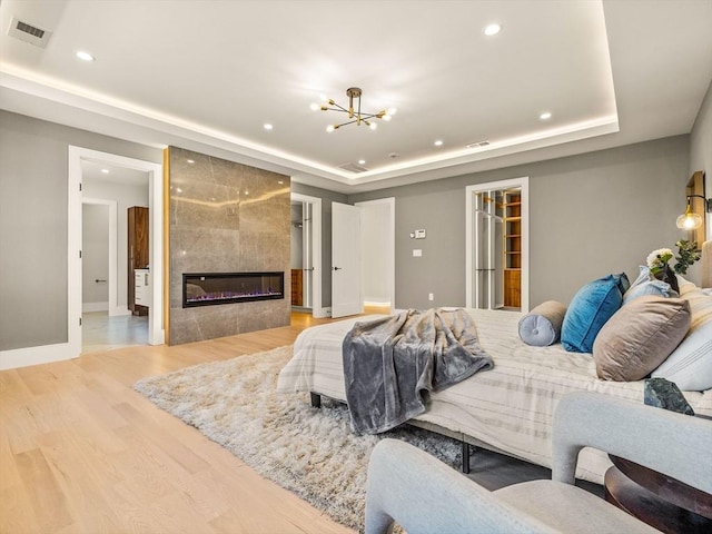 bedroom with light hardwood / wood-style floors, a tile fireplace, a raised ceiling, and an inviting chandelier