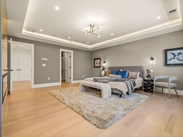 bedroom featuring light hardwood / wood-style flooring, a raised ceiling, and a notable chandelier