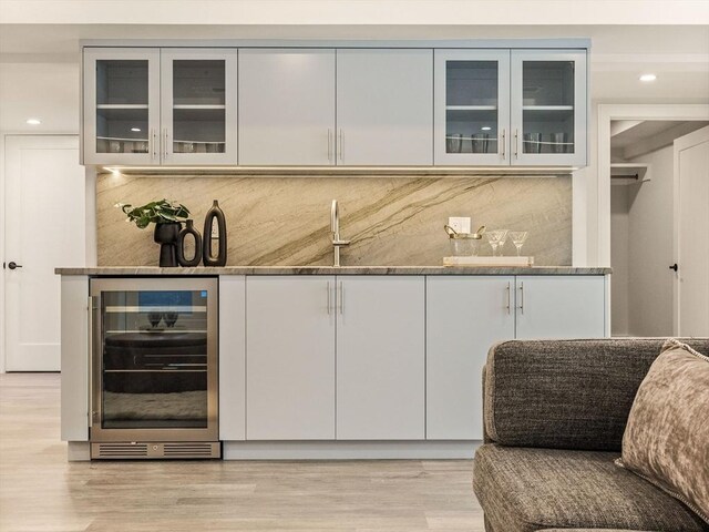 bar with sink, stone counters, light hardwood / wood-style floors, decorative backsplash, and beverage cooler