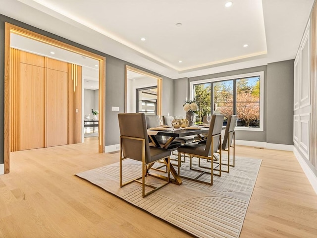 dining space with light wood-type flooring and a tray ceiling