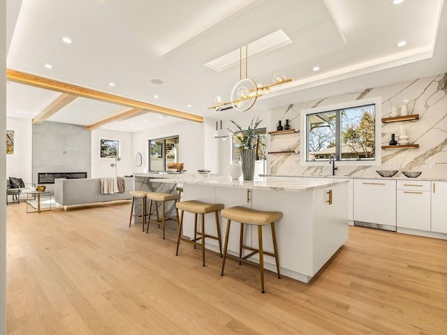 kitchen featuring hanging light fixtures, white cabinets, a kitchen bar, a center island, and a large fireplace