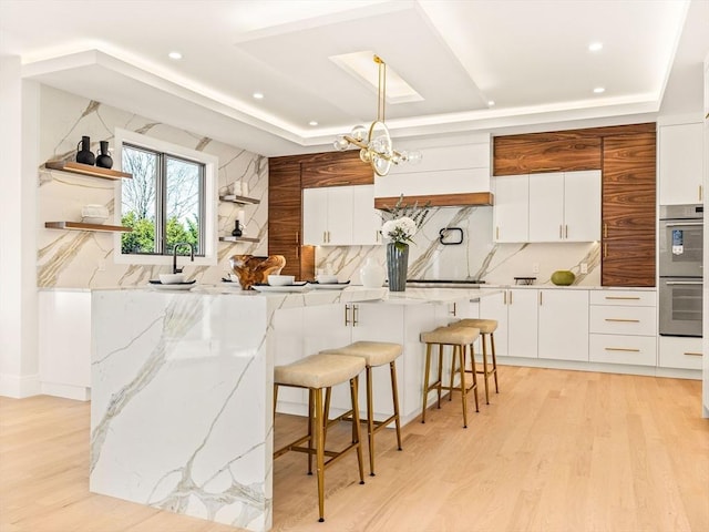 kitchen with pendant lighting, white cabinetry, tasteful backsplash, a raised ceiling, and a breakfast bar