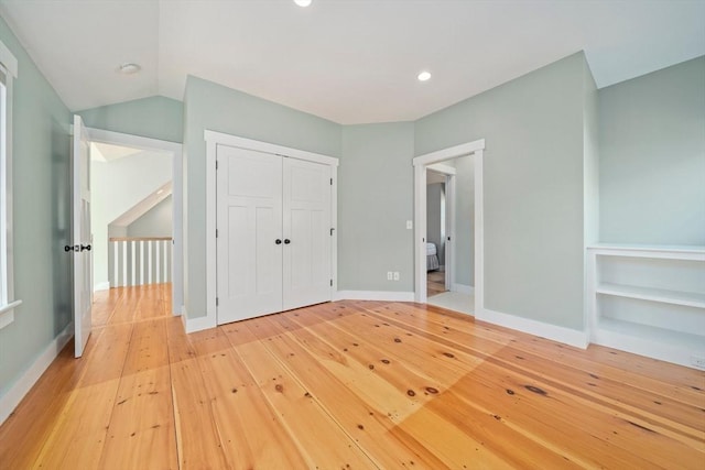 unfurnished bedroom with a closet, hardwood / wood-style floors, and vaulted ceiling