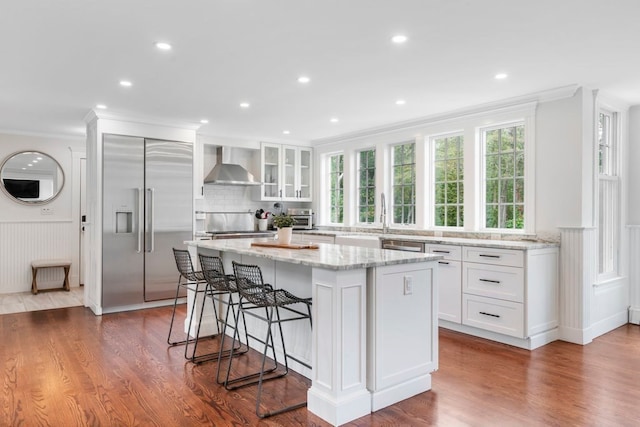 kitchen featuring a center island, wall chimney exhaust hood, dark hardwood / wood-style flooring, stainless steel built in refrigerator, and white cabinetry