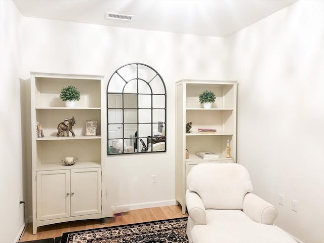 sitting room with light wood-style flooring, built in shelves, visible vents, and baseboards