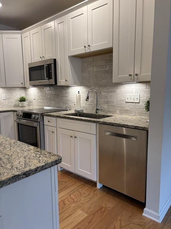 kitchen with stainless steel appliances, stone countertops, a sink, and light wood-style flooring