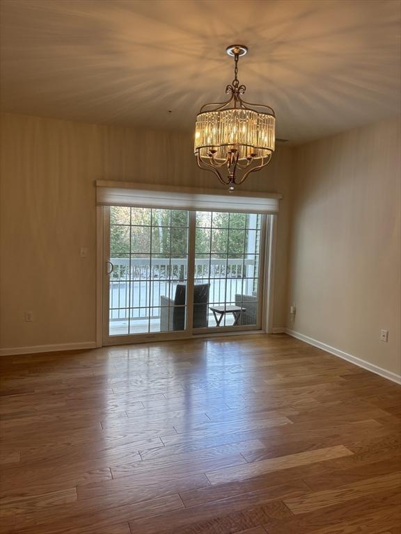 spare room with an inviting chandelier, baseboards, and wood finished floors