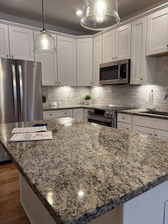 kitchen with decorative backsplash, a kitchen island, appliances with stainless steel finishes, stone counters, and a sink