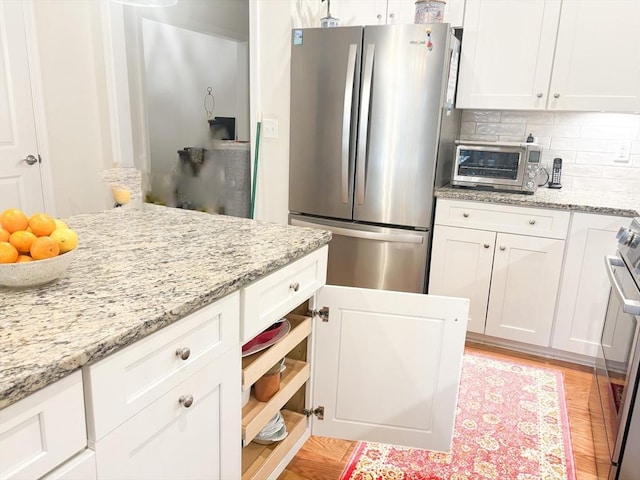 kitchen featuring a toaster, white cabinets, stove, freestanding refrigerator, and backsplash