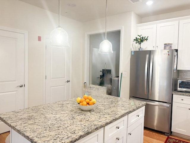 kitchen featuring a toaster, freestanding refrigerator, white cabinets, a kitchen island, and light stone countertops