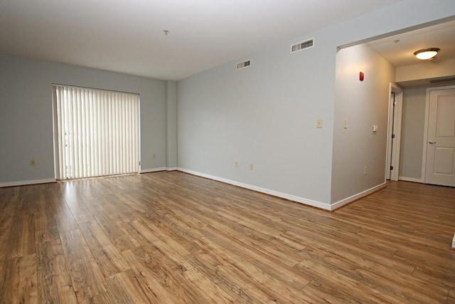 empty room featuring wood finished floors, visible vents, and baseboards