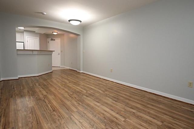 unfurnished living room with arched walkways, baseboards, and wood finished floors