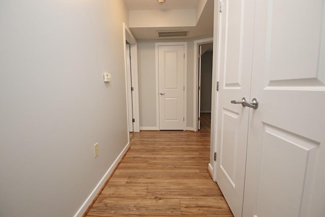 hallway featuring light wood-style floors, visible vents, and baseboards