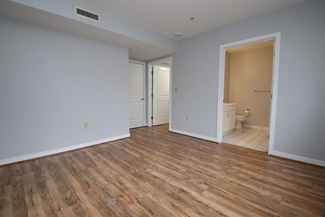 unfurnished bedroom with light wood-style flooring, baseboards, visible vents, and connected bathroom