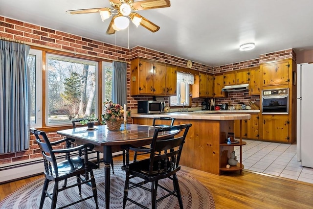 dining room featuring ceiling fan, light hardwood / wood-style flooring, sink, and brick wall