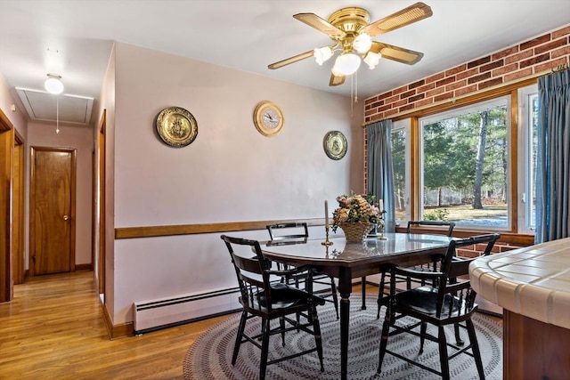 dining area with a baseboard heating unit, brick wall, ceiling fan, and light hardwood / wood-style floors