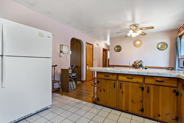 kitchen featuring ceiling fan, white refrigerator, tile countertops, and light tile patterned floors