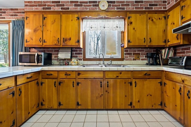 kitchen featuring brick wall, light tile patterned floors, sink, and tile countertops