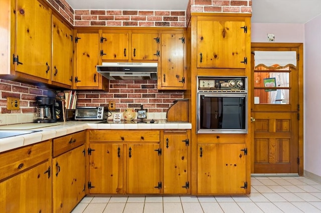 kitchen with brick wall, light tile patterned flooring, black appliances, and tile counters