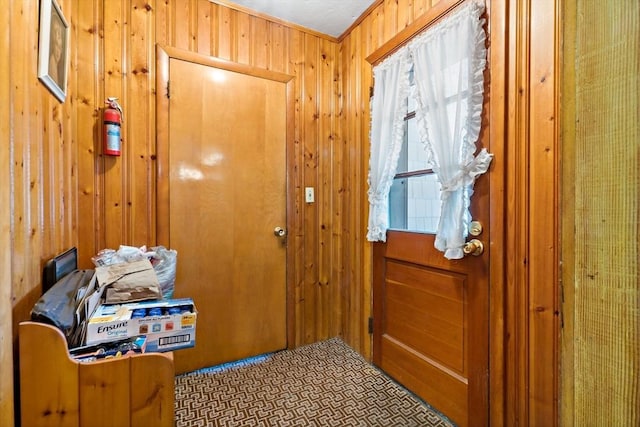 entryway with ornamental molding and wooden walls