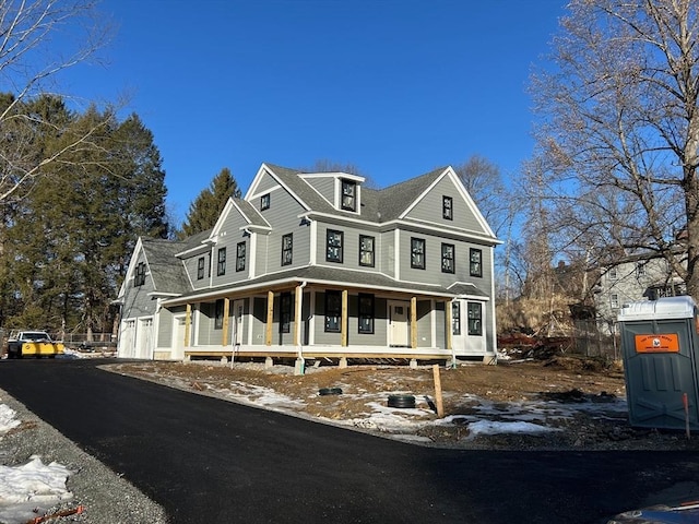 view of front facade with a shingled roof, a porch, and aphalt driveway