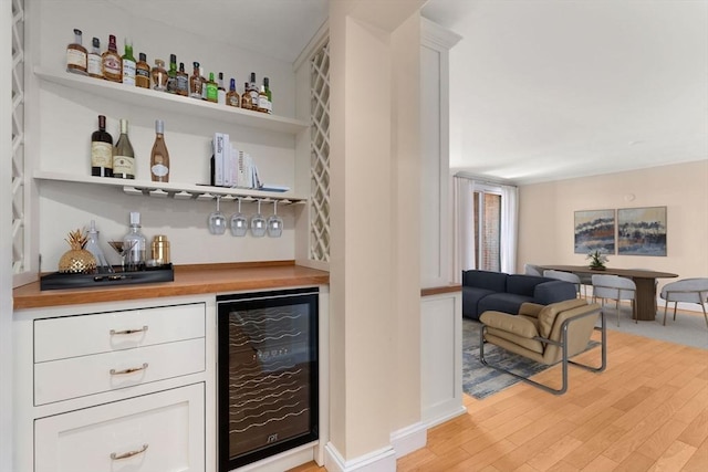 bar with wine cooler, white cabinetry, wood counters, and light hardwood / wood-style flooring