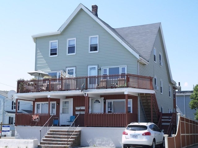 view of front of house featuring stairs, a shingled roof, a chimney, and covered porch