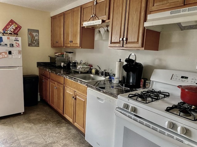 kitchen featuring brown cabinets, a sink, a textured ceiling, white appliances, and under cabinet range hood