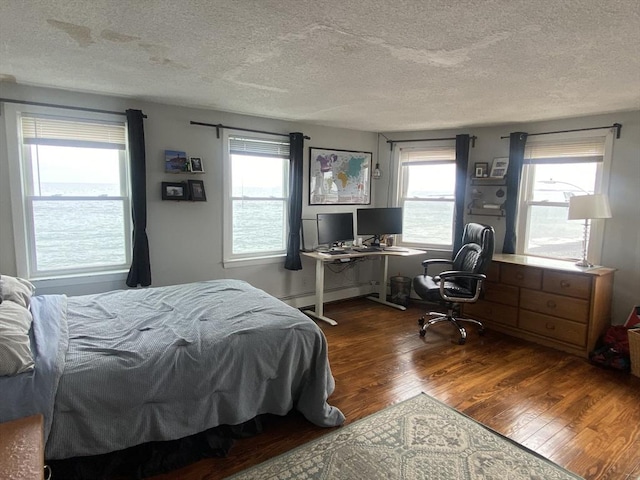 bedroom featuring a textured ceiling, a baseboard heating unit, and hardwood / wood-style floors