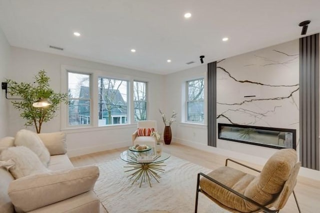 living area featuring recessed lighting, a high end fireplace, baseboards, visible vents, and light wood finished floors