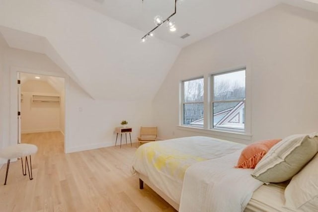 bedroom featuring visible vents, baseboards, lofted ceiling, a walk in closet, and light wood-type flooring