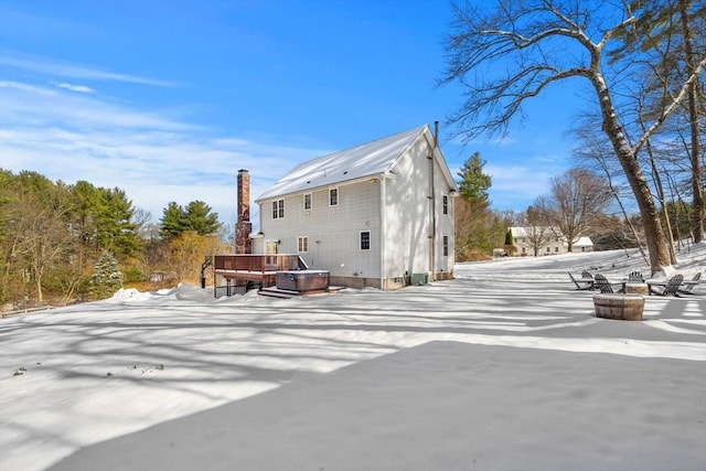 snow covered rear of property with a jacuzzi and a deck