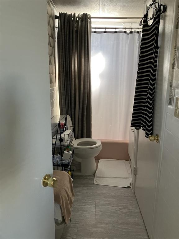 bathroom with a textured ceiling, shower / bath combo with shower curtain, and toilet