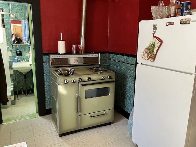 kitchen featuring light tile patterned floors, stove, tile walls, white fridge, and sink