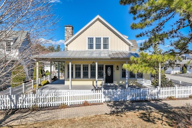 rear view of property with metal roof, a porch, a fenced front yard, board and batten siding, and a standing seam roof