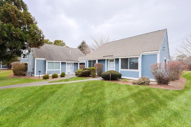 view of front of home featuring a front yard, cooling unit, and roof with shingles