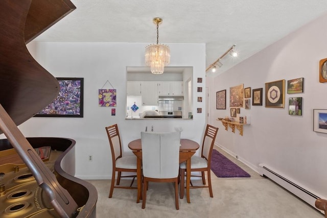 dining space featuring a baseboard heating unit, a chandelier, light colored carpet, rail lighting, and baseboards