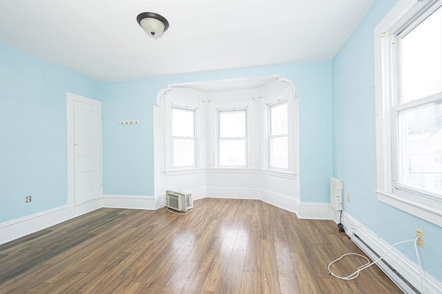 empty room featuring dark wood finished floors, baseboard heating, and a wealth of natural light