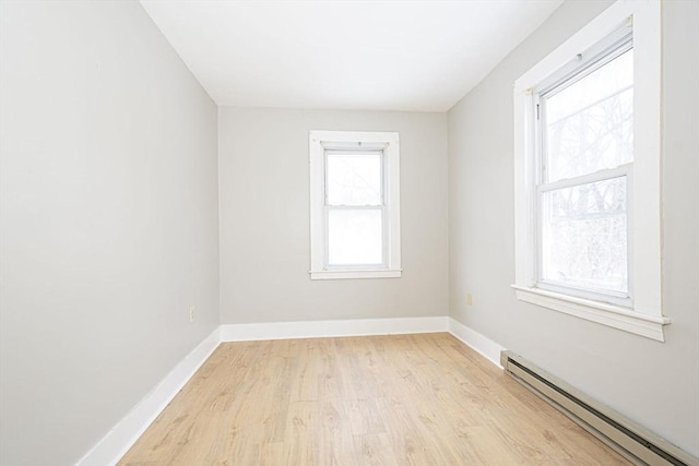 spare room featuring a baseboard heating unit, light wood finished floors, and baseboards