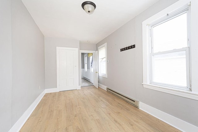 unfurnished room featuring a baseboard heating unit, light wood finished floors, and baseboards